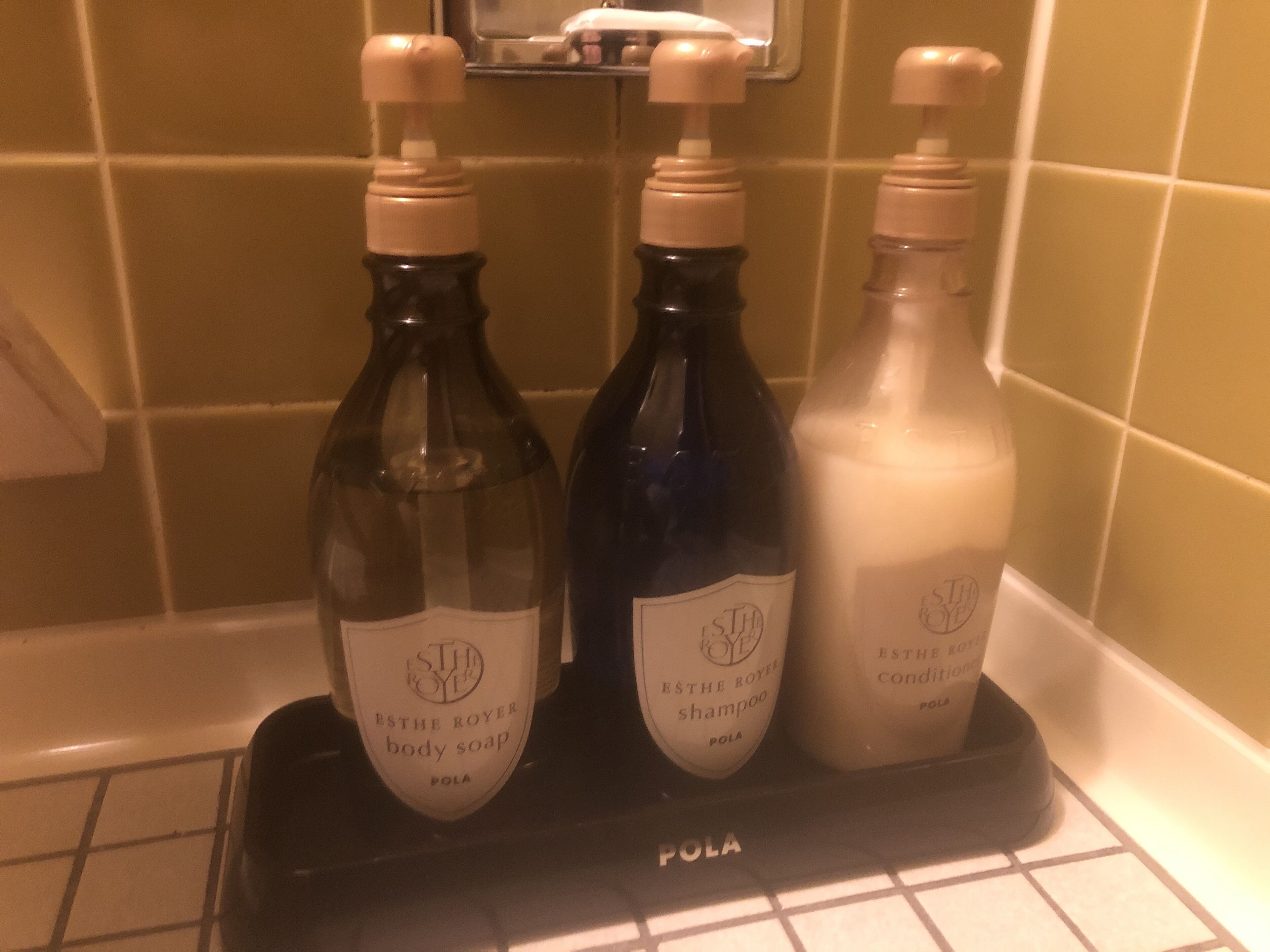 Three bottles of body soap and shampoo on a black tray in a bathroom.