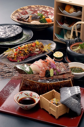 A variety of traditional Japanese dishes arranged on a table, including sushi, sashimi, and a bowl of rice with vegetables.