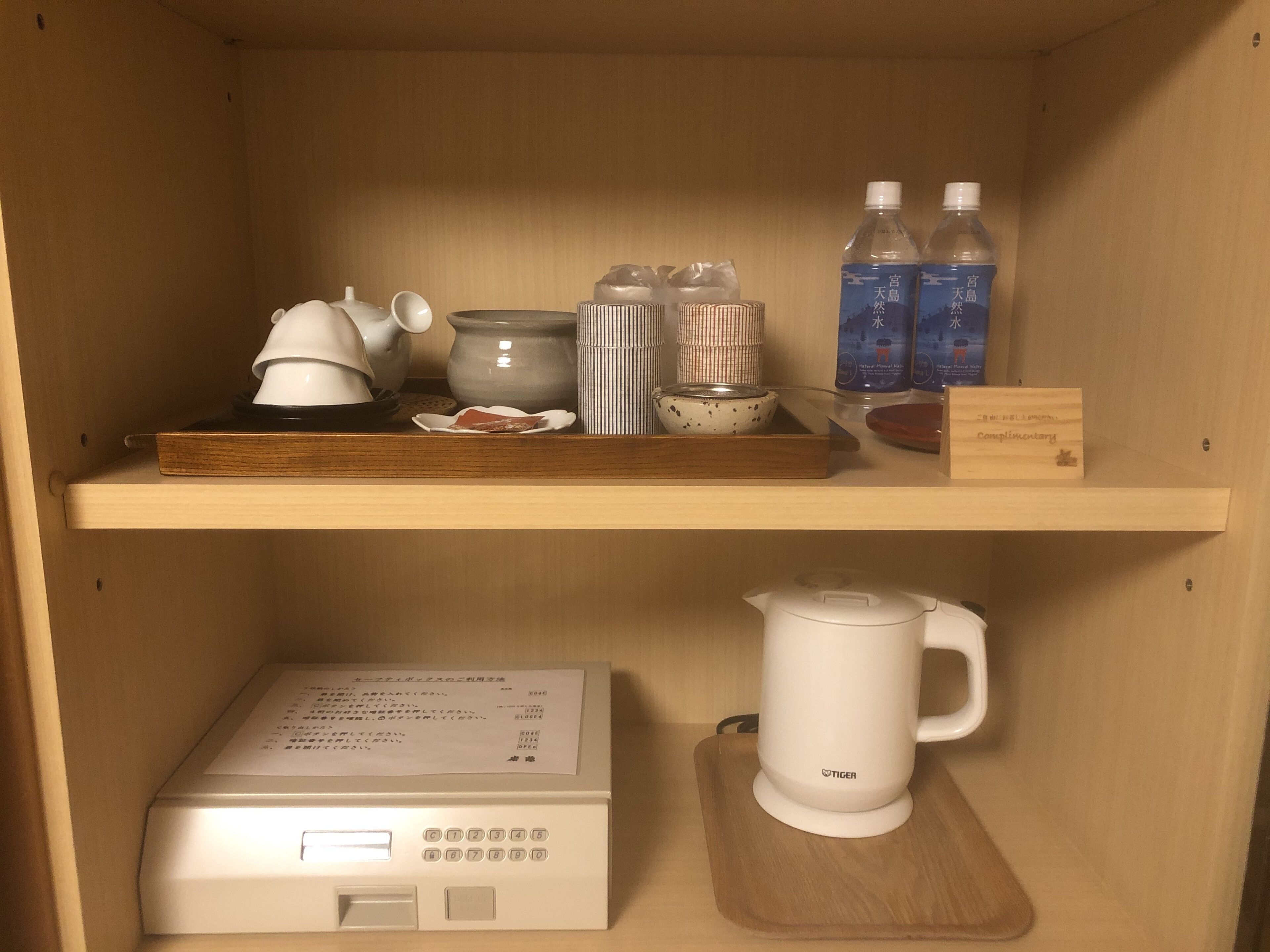 A shelf with a teapot, cups, a kettle, and bottled water.