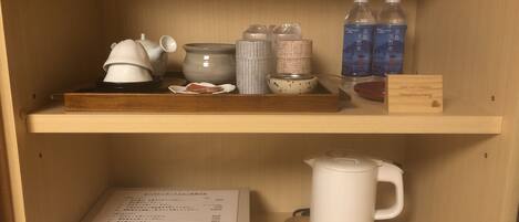 A shelf with a teapot, cups, a kettle, and bottled water.
