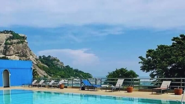 A pool area with slides, lounge chairs, and a view of a rocky cliff. - Blue Wave Hotel Hua Hin (Hua Hin)