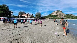 A beach with people walking and standing, umbrellas, and a building in the background. - Blue Wave Hotel Hua Hin (Hua Hin)