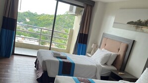 A hotel room with two beds, a large window with a view of greenery, and a ceiling fan. - Blue Wave Hotel Hua Hin (Hua Hin)
