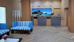 A reception area with a blue-striped sofa, a wooden reception desk, and a wall-mounted TV displaying a scenic landscape. - Blue Wave Hotel Hua Hin (Hua Hin)
