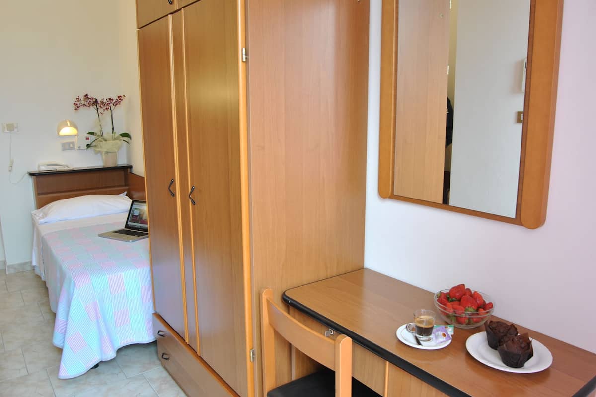 A bedroom with a bed, a desk, a mirror, a laptop, a bowl of strawberries, and a plate of muffins.