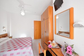 Una habitación de hotel con una cama, un escritorio con una silla, un armario, un espejo y un televisor en la pared.
