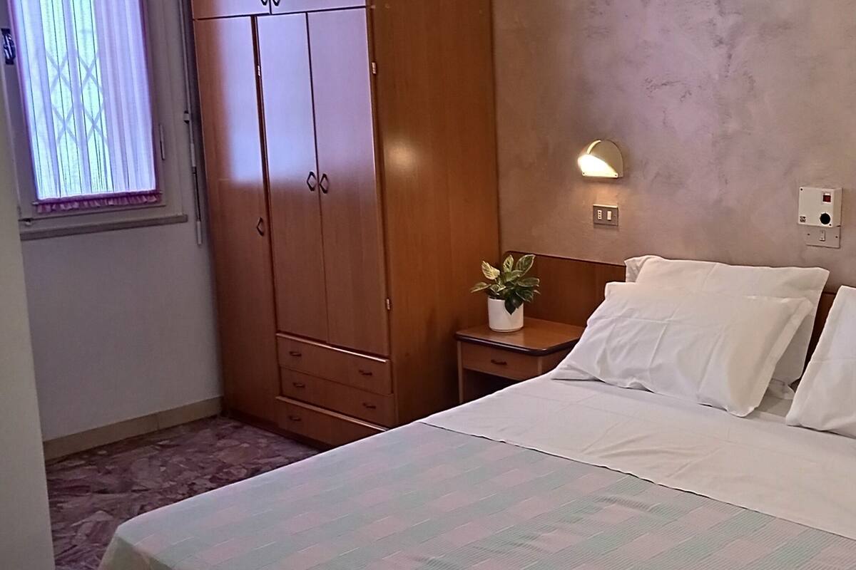 A bedroom with a bed, wooden wardrobe, bedside tables, a potted plant, and wall-mounted lights.