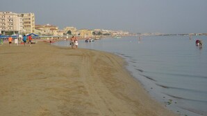 A beach with a sandy shore, buildings in the background, and boats on the water. - Hotel Samoa (Rimini)