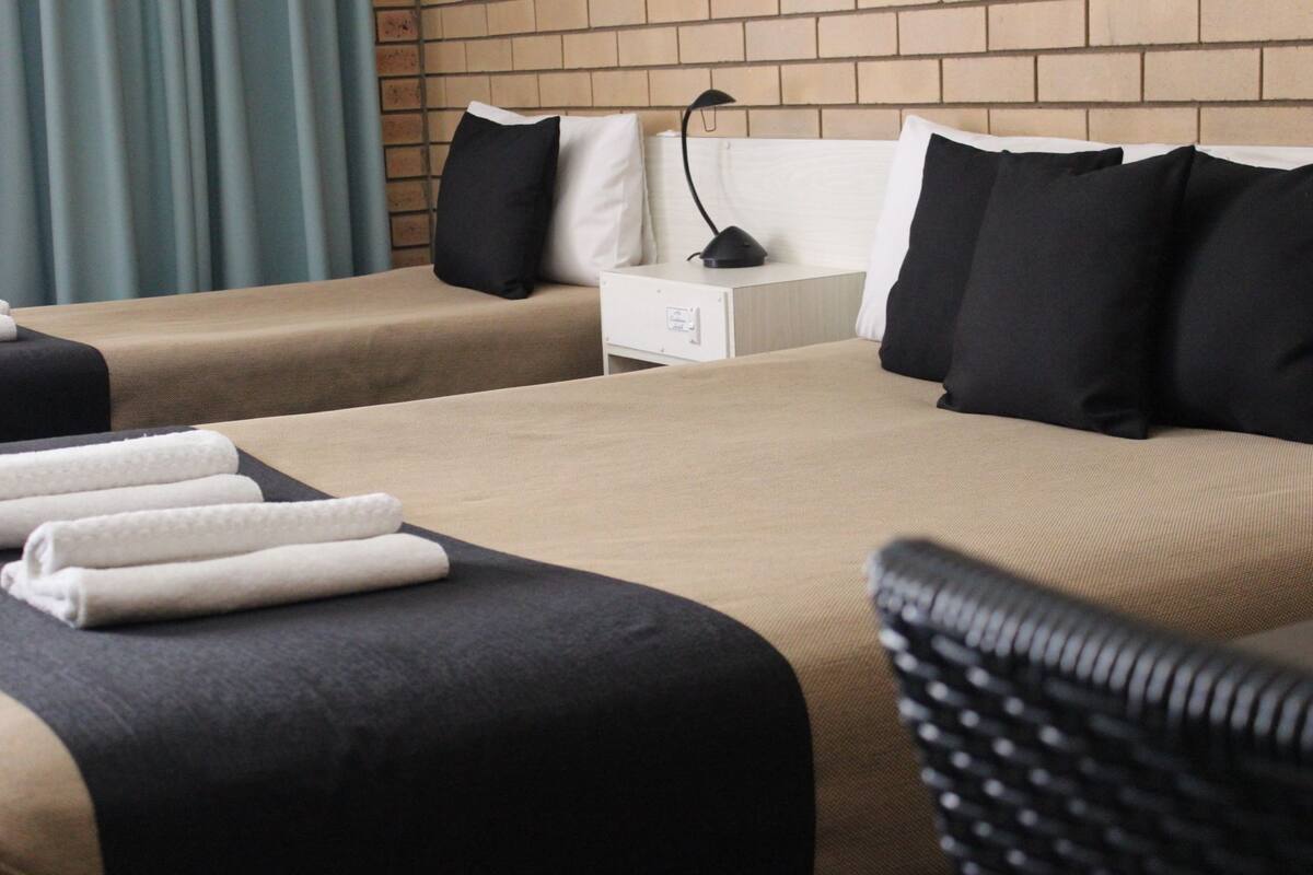 A hotel room with two beds, a nightstand, a lamp, and a chair.