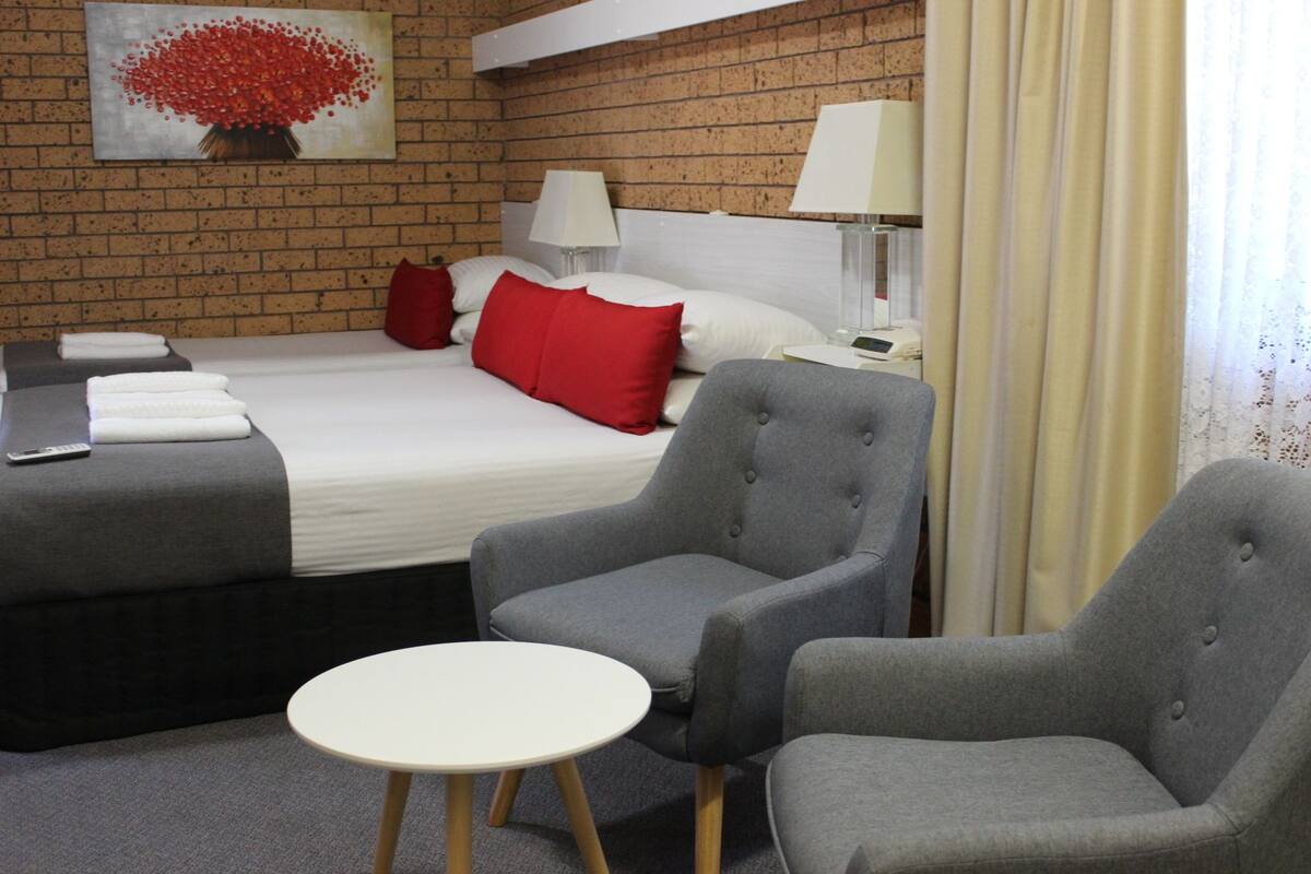 A hotel room with a bed, two armchairs, a small round table, a painting on the wall, and a lamp.