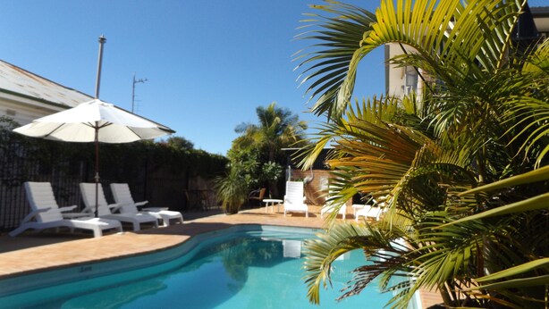 A swimming pool with lounge chairs and umbrellas, surrounded by palm trees and a fence. - Golden Harvest Motor Inn (Moree)