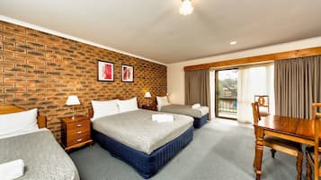 A hotel room with two beds, a wooden dining table, a brick wall, and a balcony with curtains.