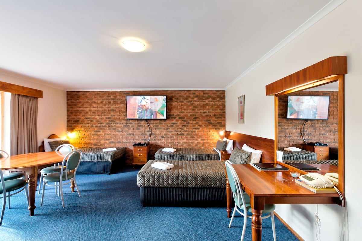 A hotel room with a brick wall, two beds, a desk, and a TV.