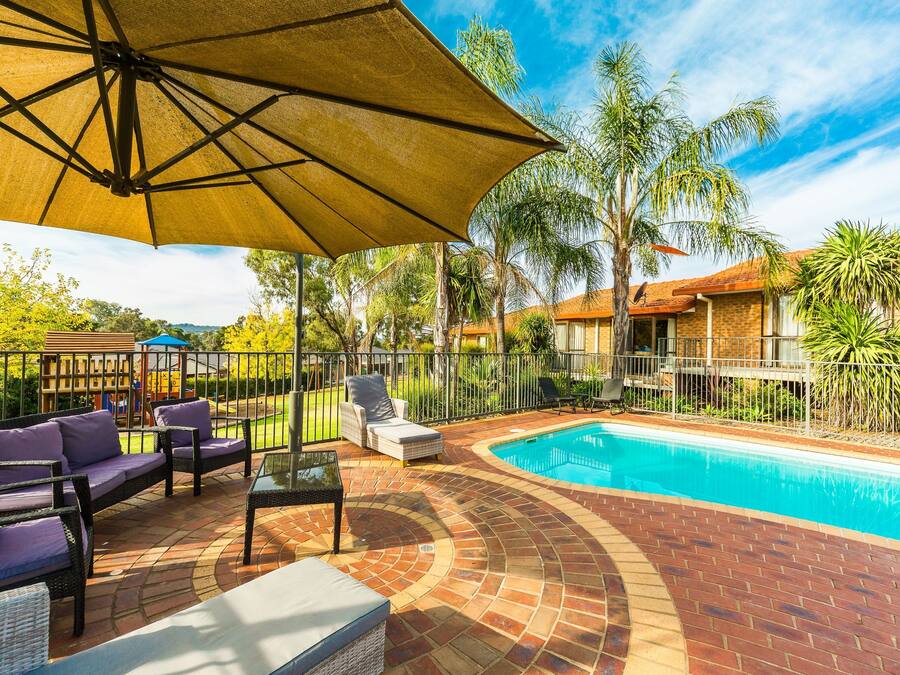 A poolside area with a brick patio, lounge chairs, and an umbrella.