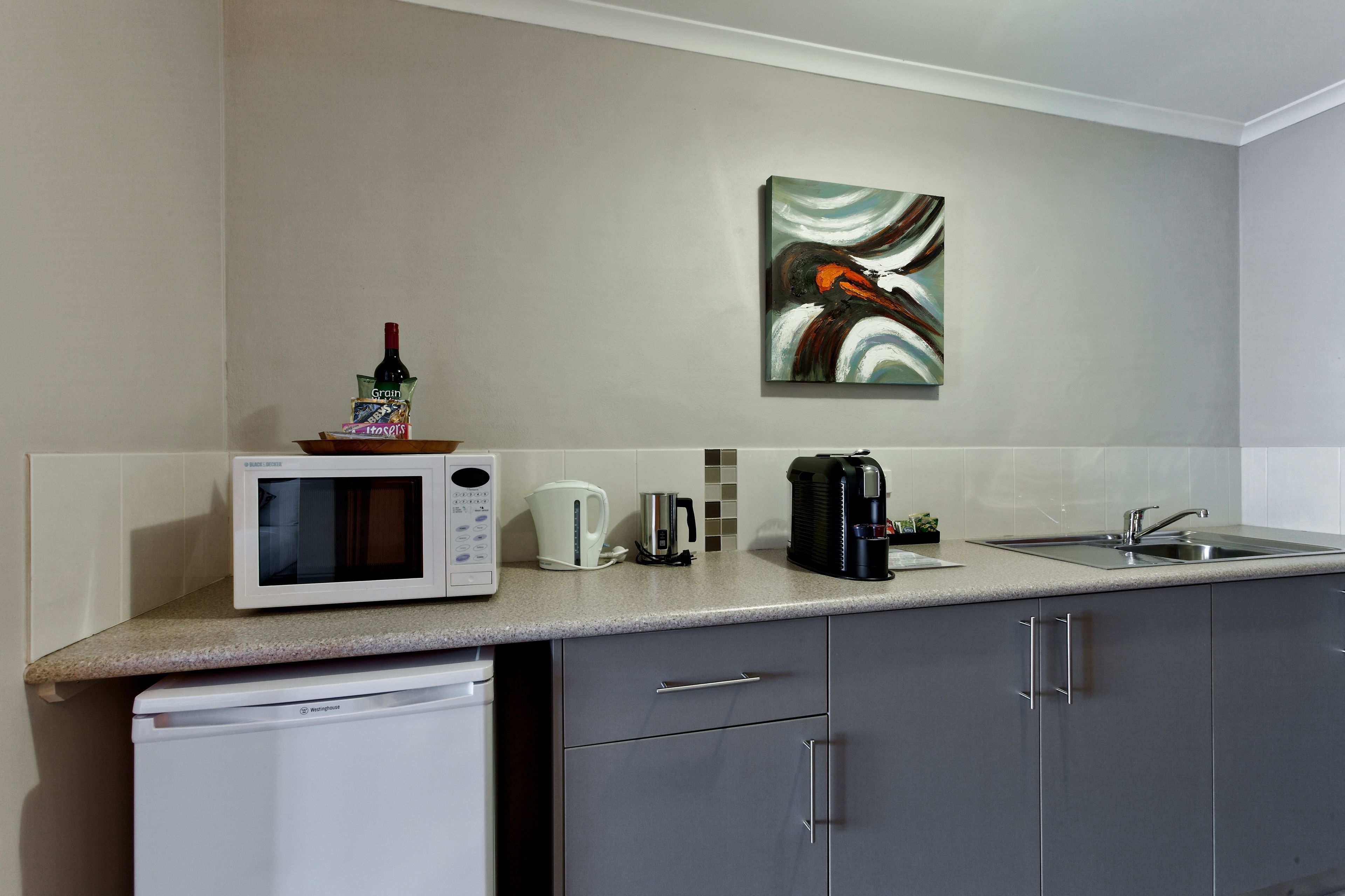 Una cocina moderna con microondas, cafetera, hervidor y lavabo.