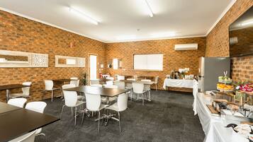 A conference room with brick walls, white chairs, tables, and a buffet area with food and drinks.