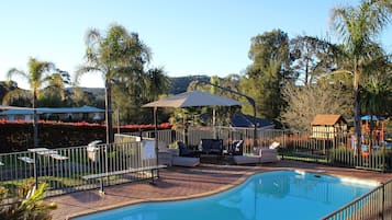 Una piscina con sillas de descanso y sombrillas, rodeada por una valla y palmeras.