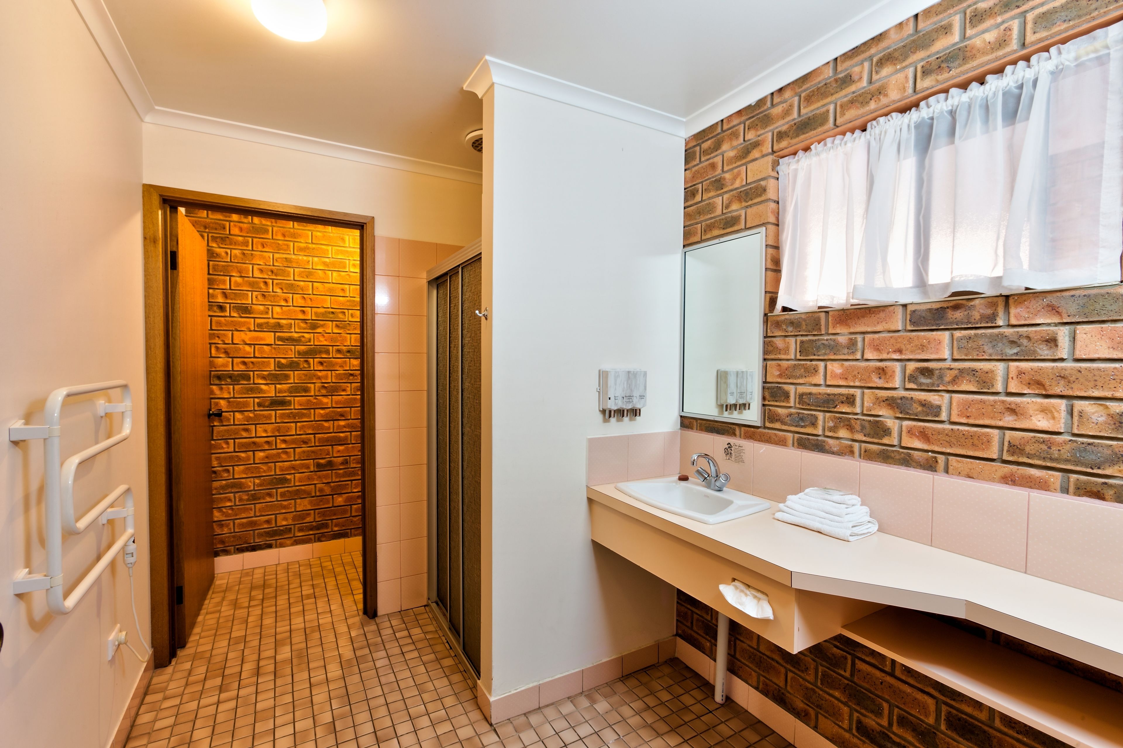 A bathroom with a brick wall, a white sink, a mirror, and a towel rack.
