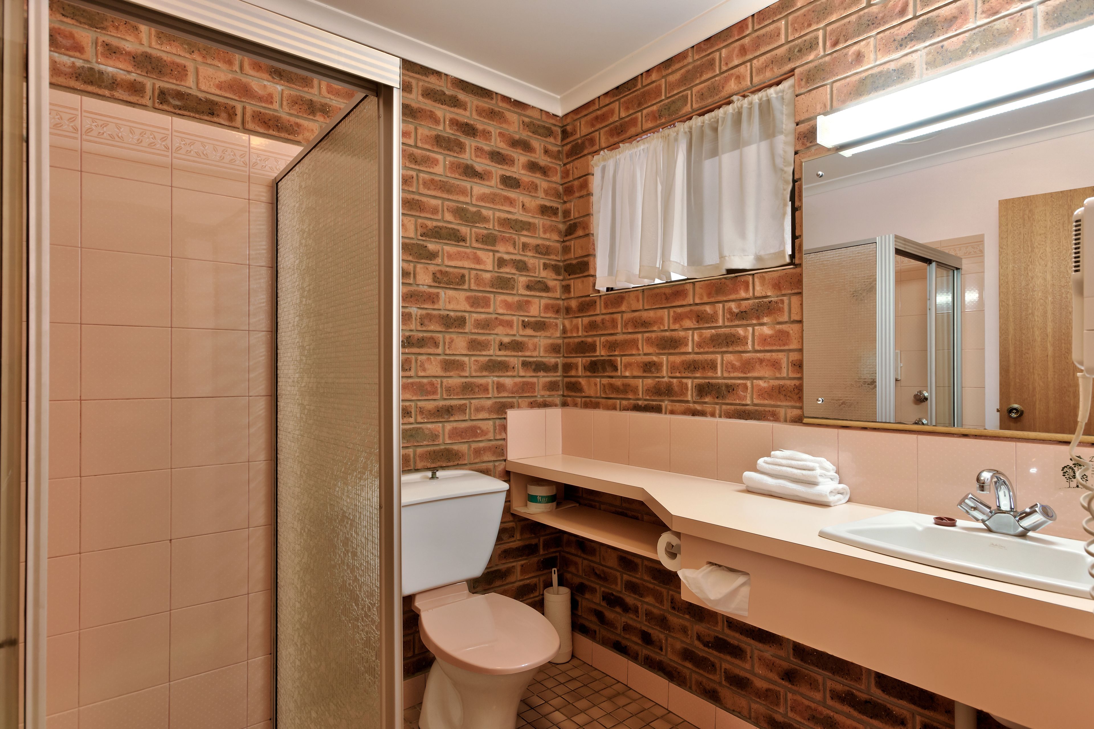 Un baño con pared de ladrillo, inodoro, lavamanos y ducha.