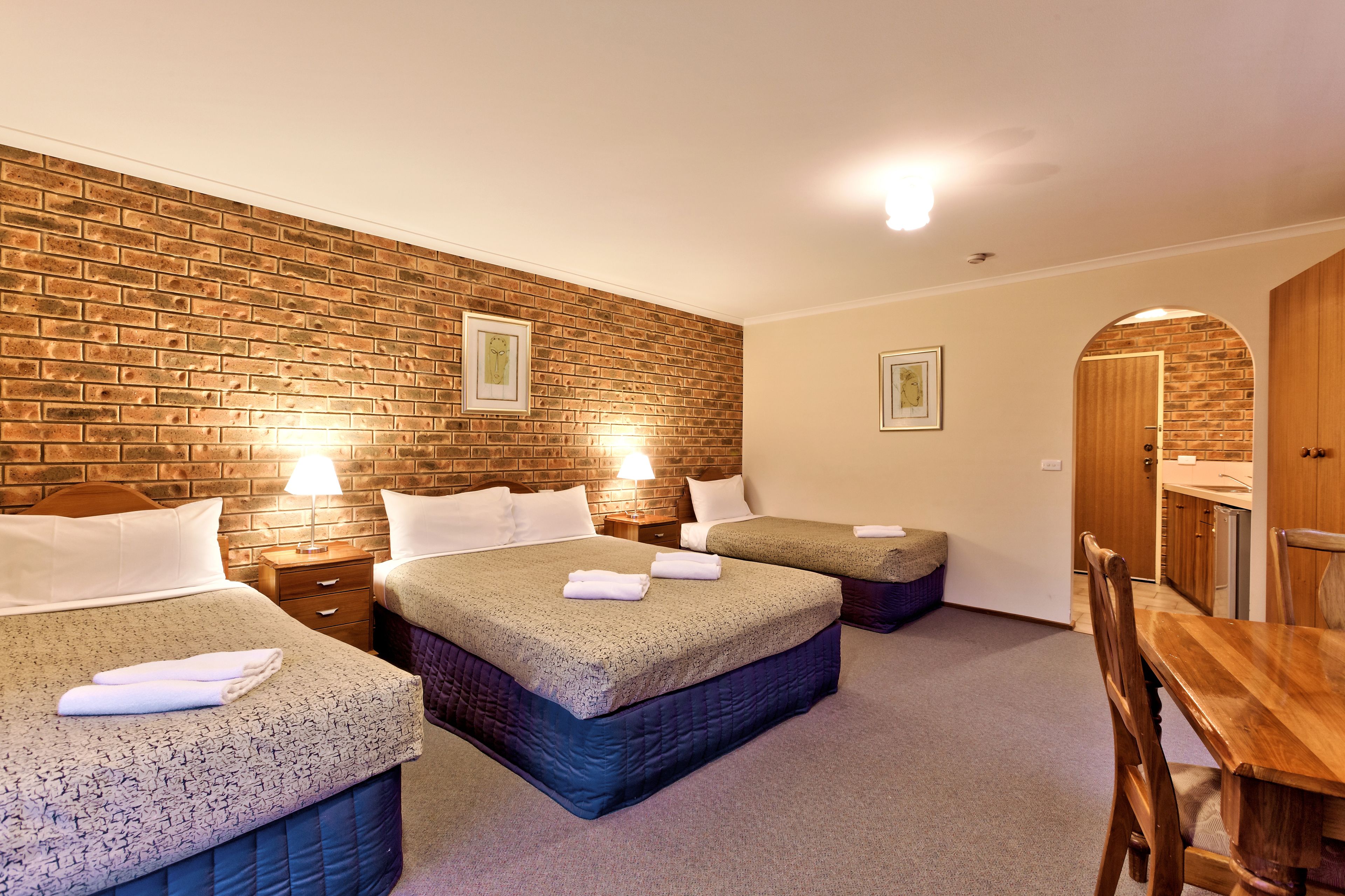 A hotel room with three beds, a wooden dining table, and a brick wall.