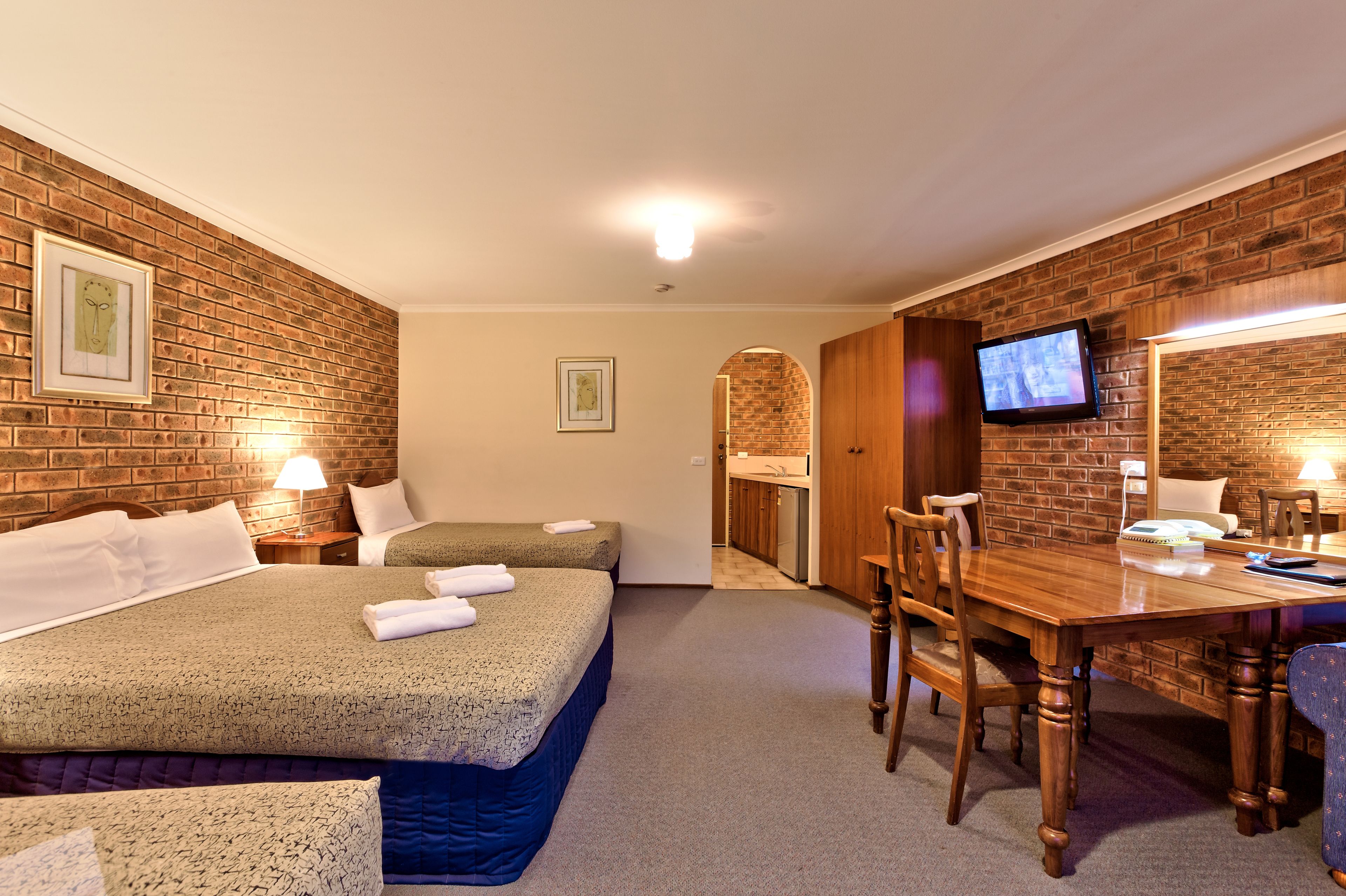 Een hotelkamer met twee bedden, een houten eettafel, stoelen, een televisie en een kitchenette op de achtergrond.