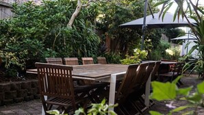 An outdoor dining area with a wooden table and chairs, surrounded by lush greenery and a brick floor. - Murwillumbah Motor Inn (Murwillumbah)