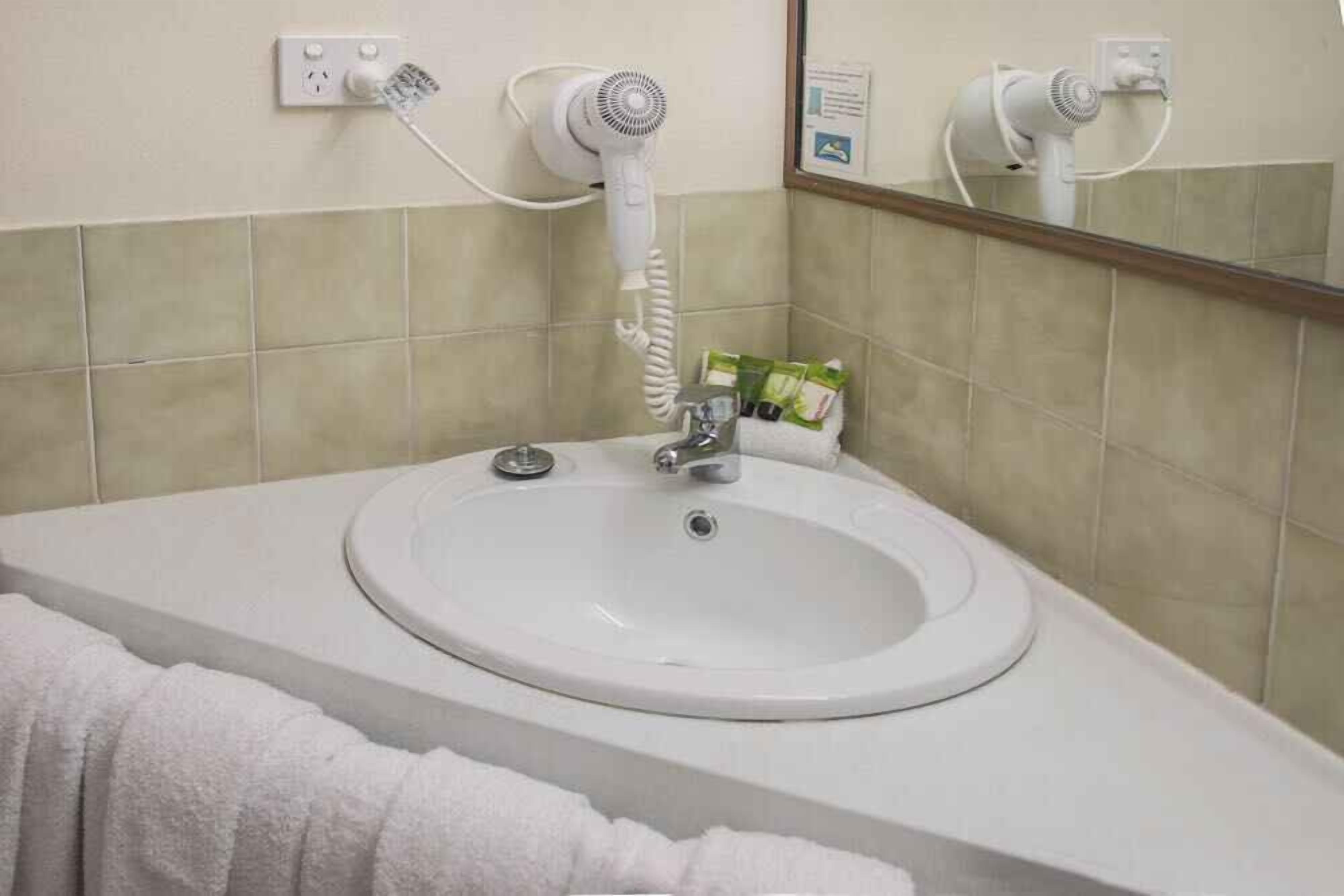 Une salle de bain avec un lavabo blanc, un miroir et un sèche-cheveux fixé au mur.