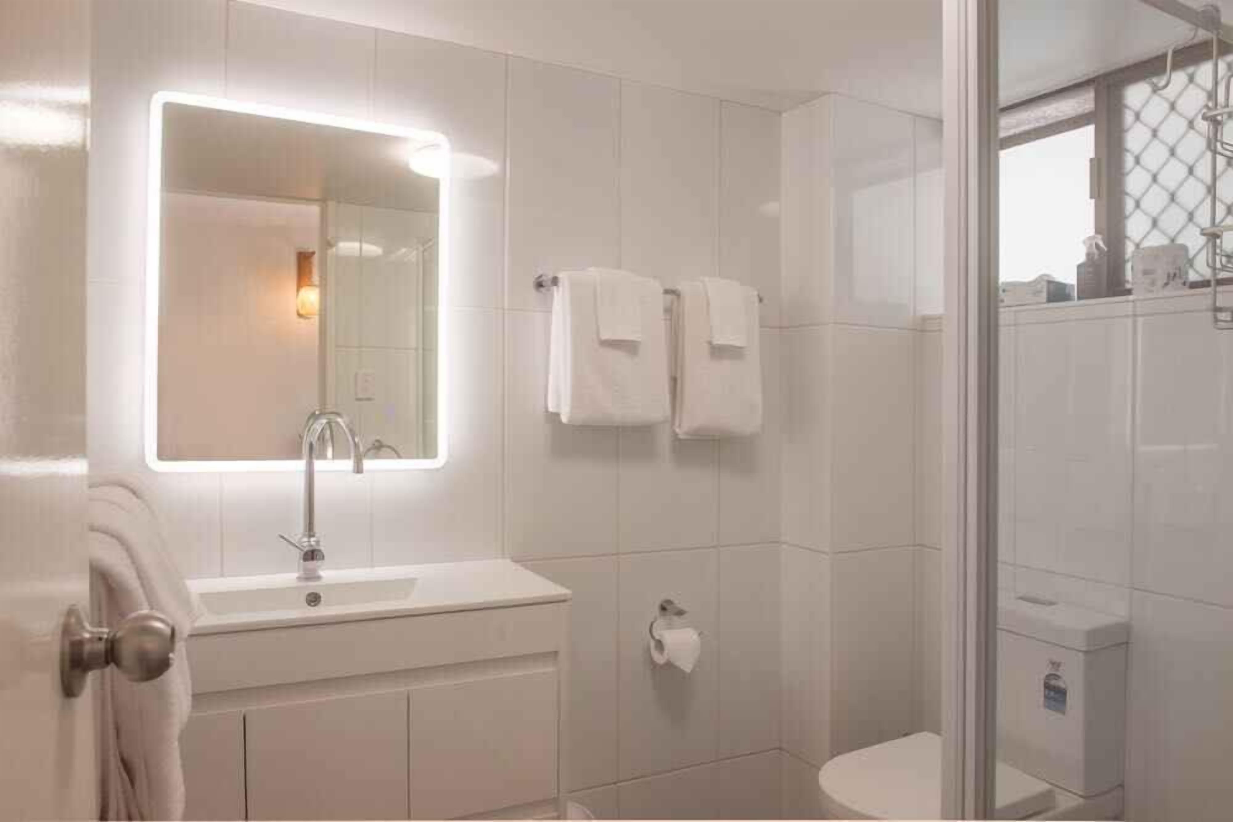 Une salle de bain moderne avec une douche à parois de verre, un grand miroir et un lavabo blanc.