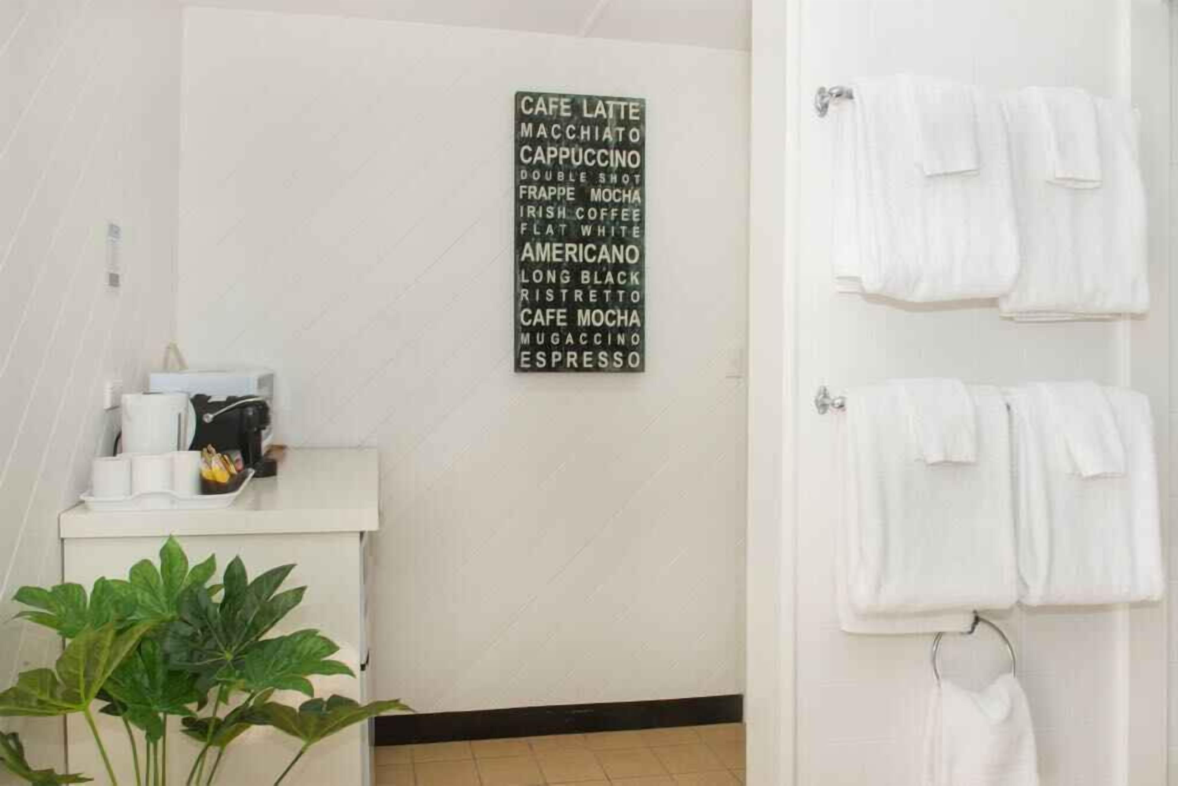Un baño con un cartel en la pared que enumera tipos de café, un lavamanos con artículos de aseo y toallas colgadas en un perchero.