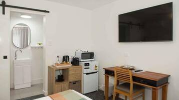 A compact hotel room with a bed, a desk with a chair, a microwave, a small refrigerator, a sink, and a large mirror.
