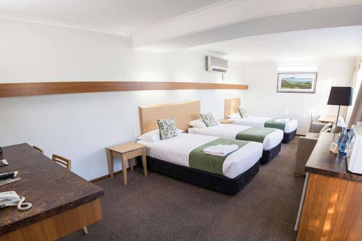 A hotel room with three beds, a desk, a chair, a small table, and a picture on the wall.