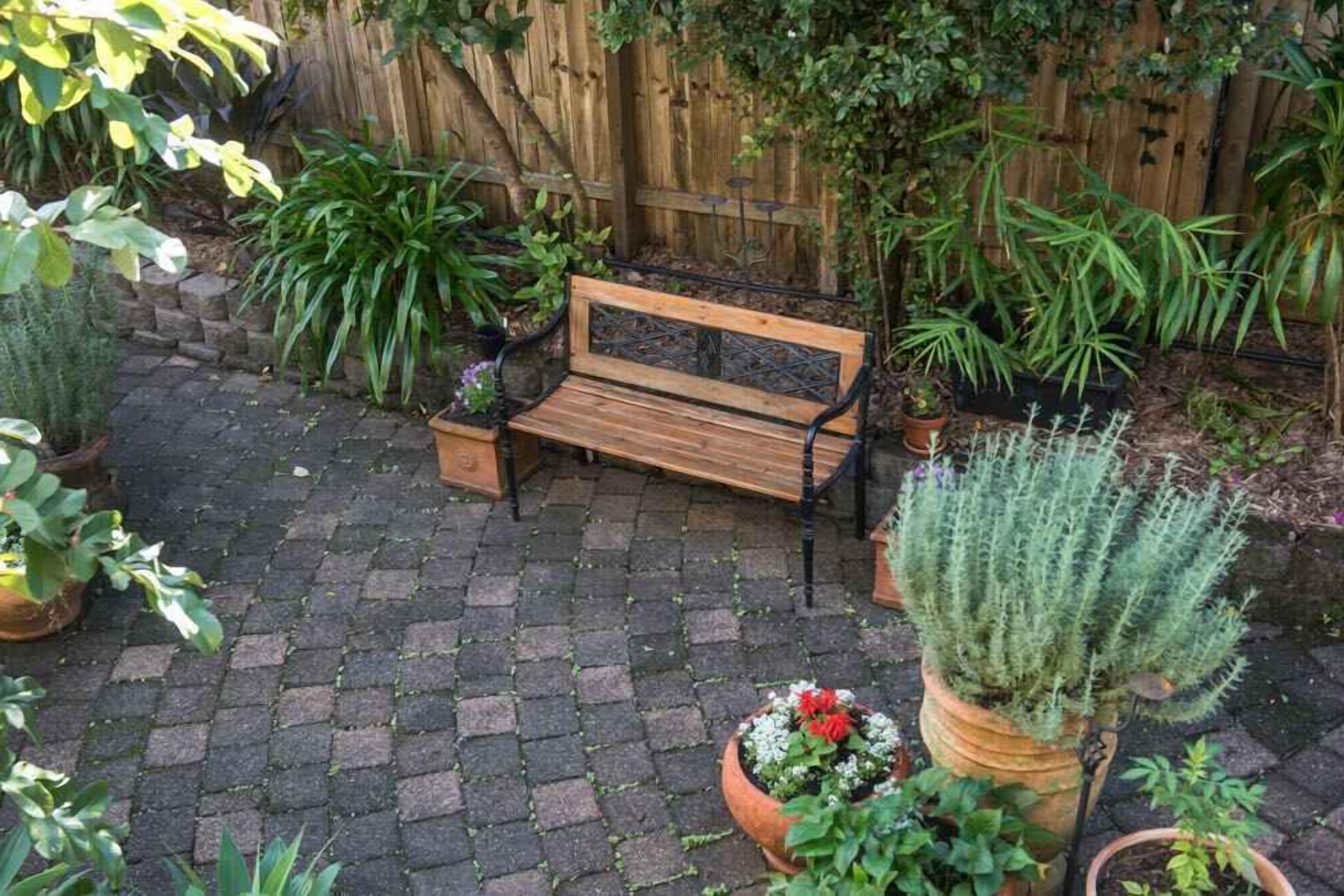 En træbænk i en have med plantekasser og et træhegn i baggrunden.