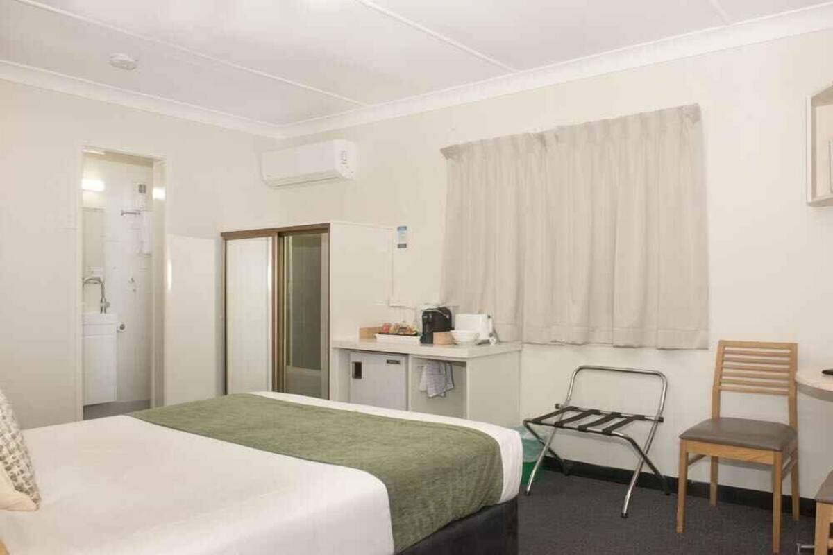 A hotel room with a bed, a desk with a chair, a small kitchenette, and a window with curtains.