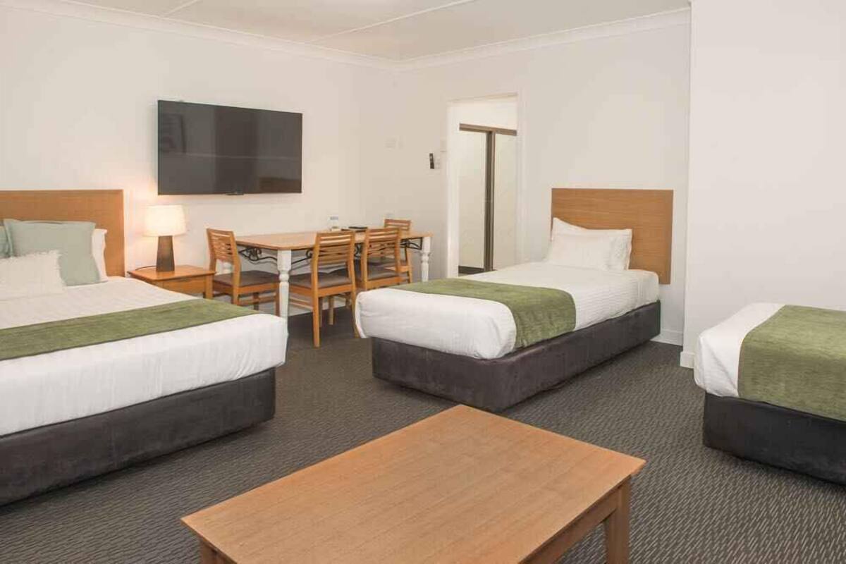 A hotel room with two beds, a TV, a dining table with chairs, and a wooden table.