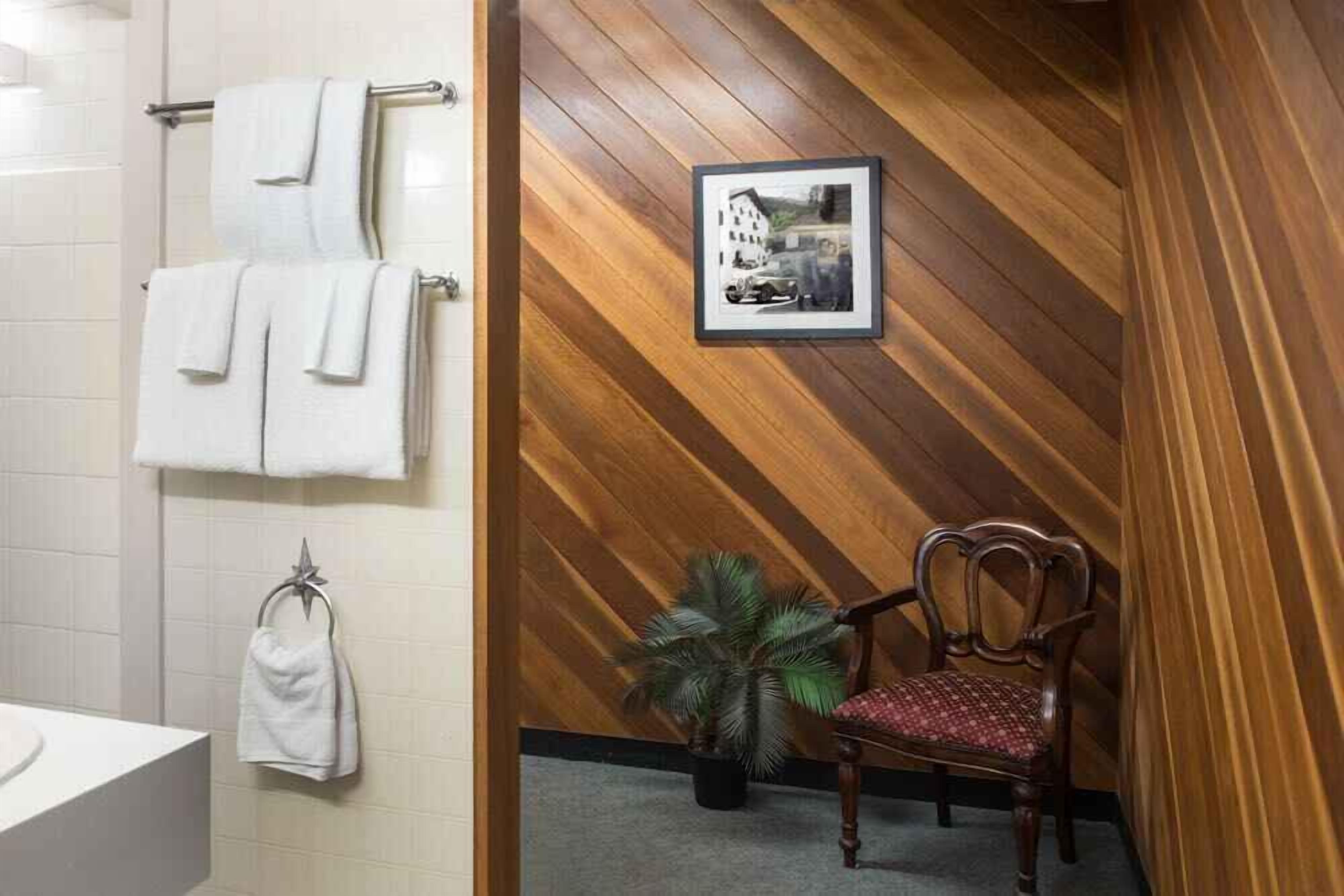 Un baño con pared de madera, un cuadro enmarcado, una silla y una planta en maceta.