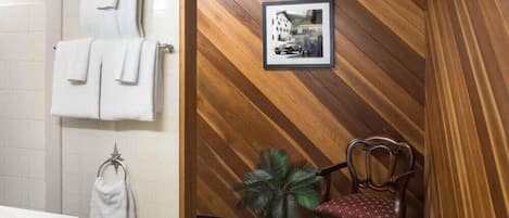 Un baño con pared de madera, un cuadro enmarcado, una silla y una planta en maceta.