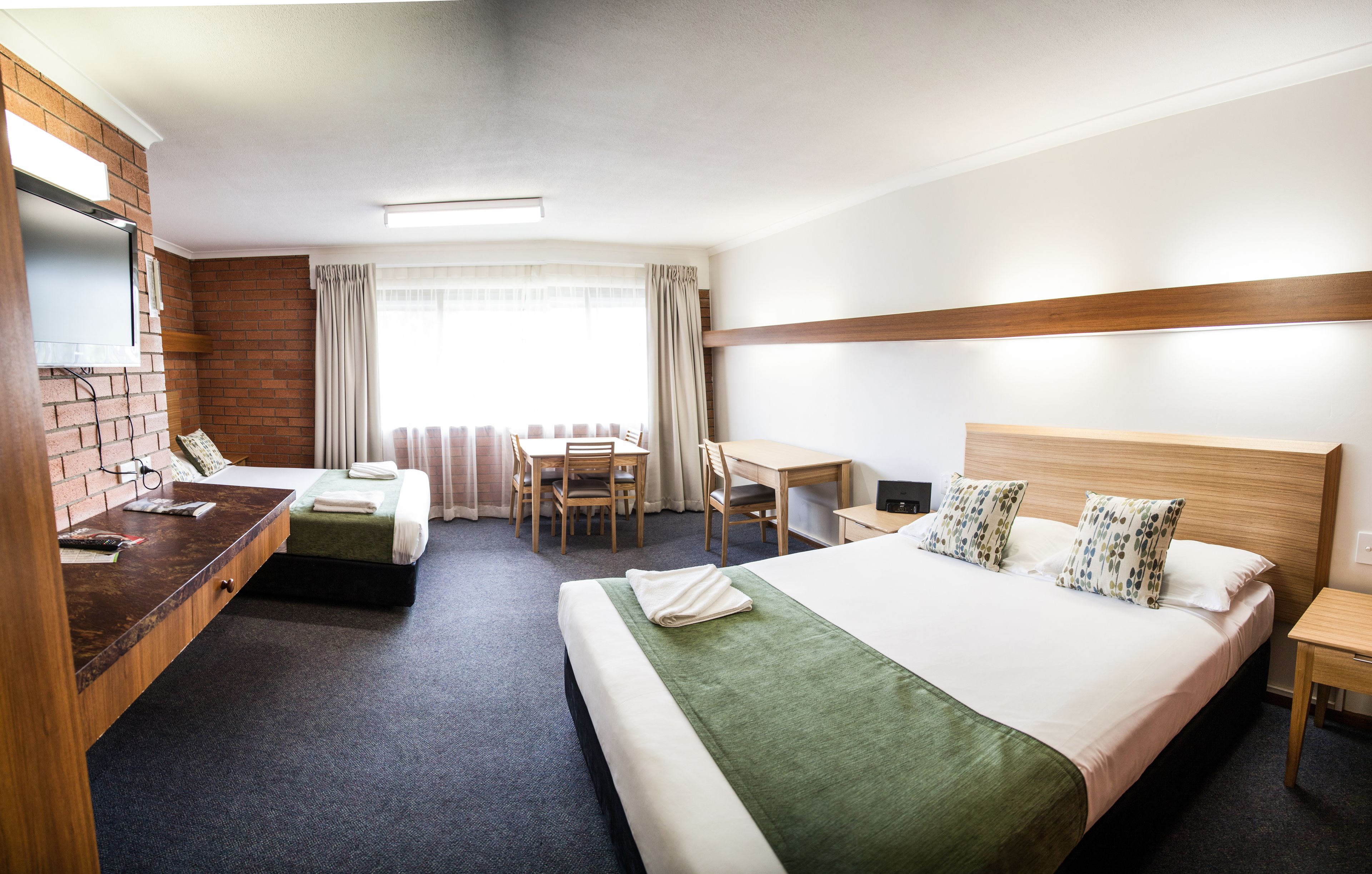 A hotel room with a bed, a desk, a chair, a small table, and a TV.