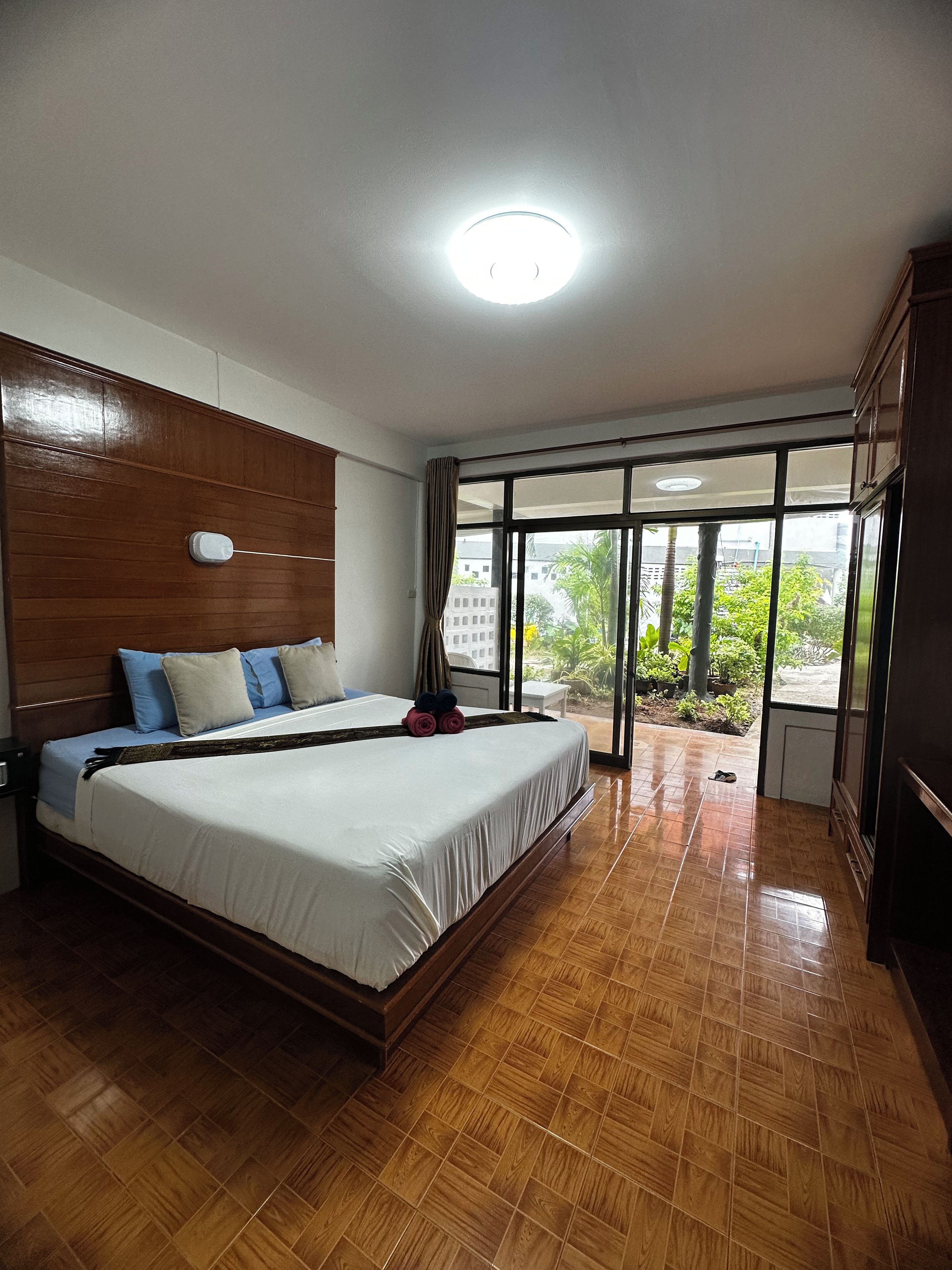A hotel room with a large bed, wooden headboard, and a view through a large window.