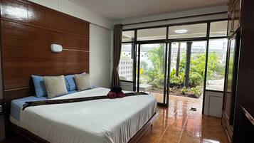A hotel room with a large bed, wooden headboard, and a view through a large window.