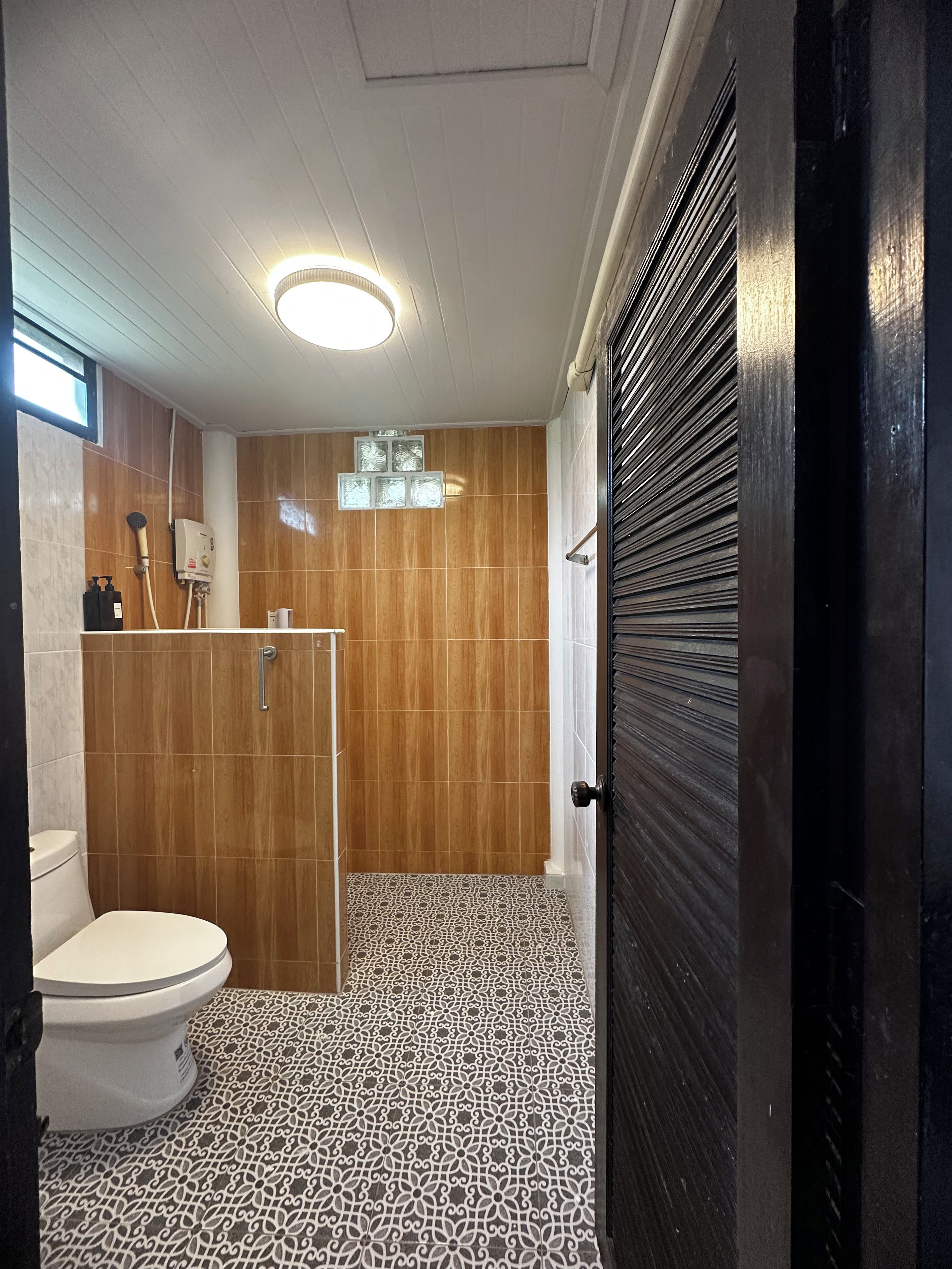 A bathroom with a toilet, shower, and patterned floor tiles.
