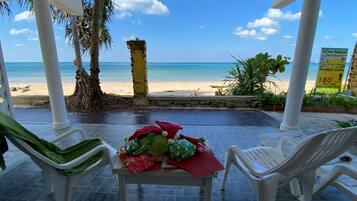 A covered outdoor seating area with a table set for two, overlooking a beach.
