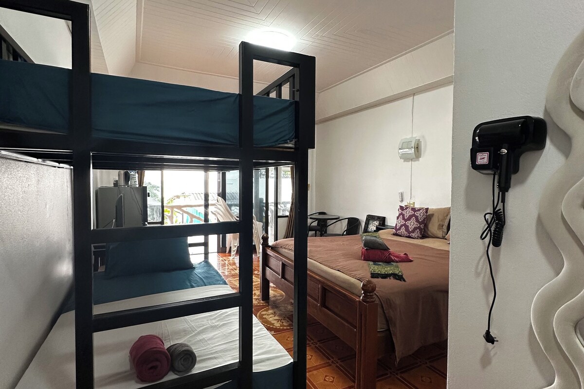 A room with a bunk bed, a desk, a chair, a sofa, and a wall-mounted hairdryer.