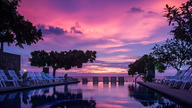 A poolside area with lounge chairs and a view of the sunset over the ocean. - Lanta Garden Home (Ko Lanta)