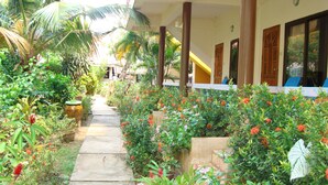 A pathway leading to a building with a covered porch, surrounded by lush greenery and flowering plants. - Lanta Garden Home (Ko Lanta)