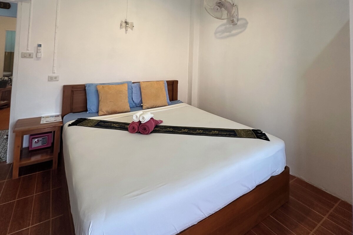 A hotel room with a bed, a bedside table, a wall-mounted fan, and a ceiling light.