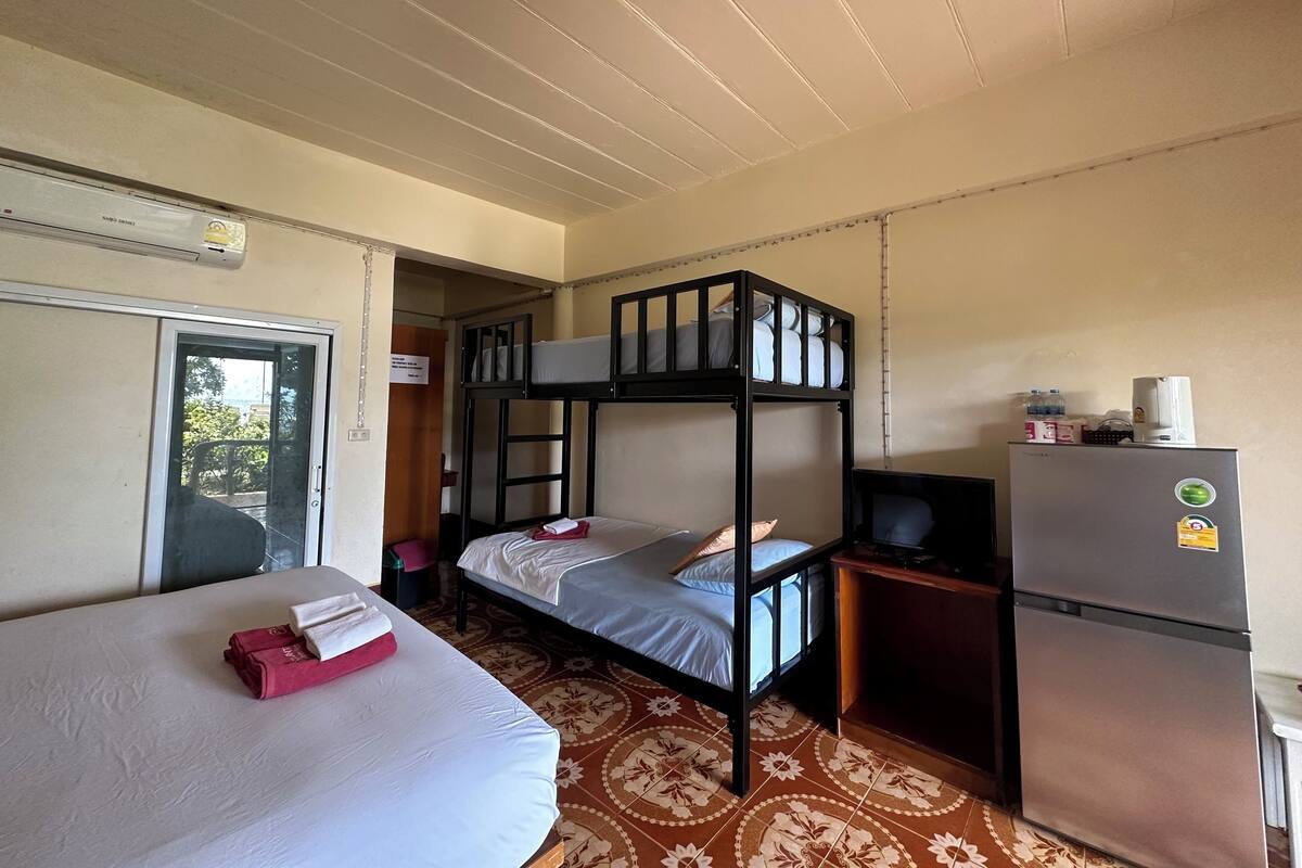 A room with bunk beds, a refrigerator, a small table, and a door leading to a balcony.