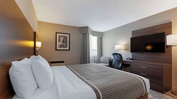 A hotel room with a large bed, a desk with a chair, a television, and a wardrobe.
