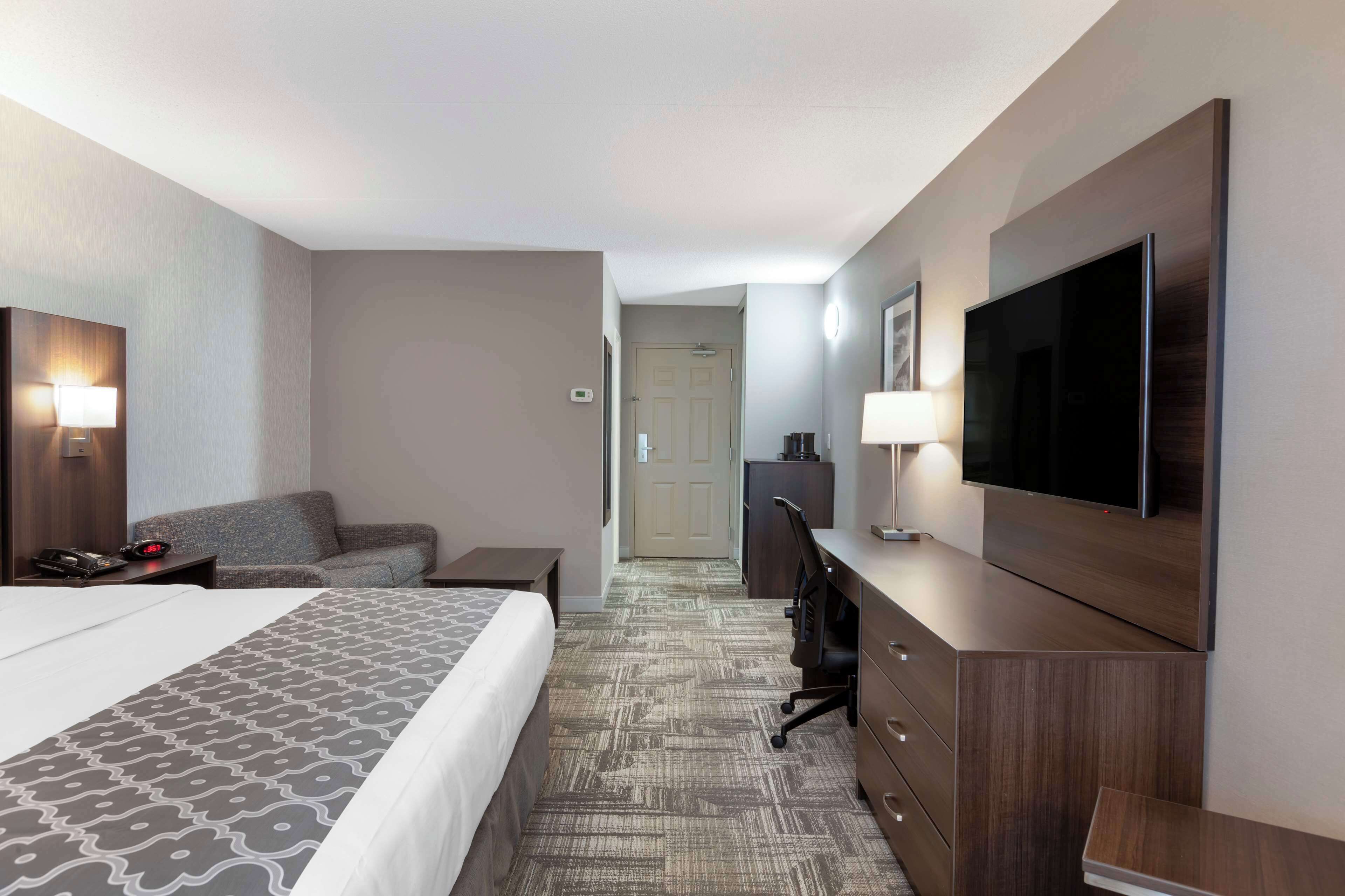 A hotel room with a large bed, a desk with a flat-screen TV, a sofa, and a lamp.