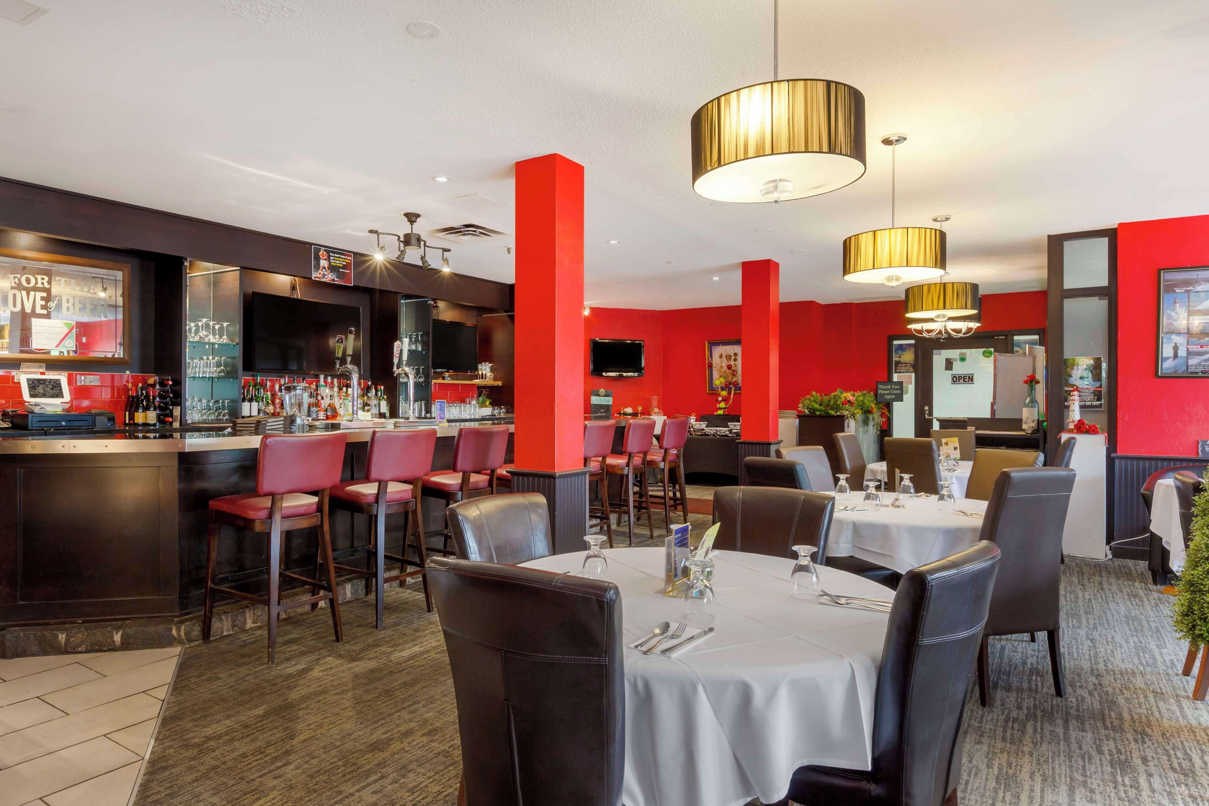 Un restaurant aux murs rouges, avec un coin bar et des tables dressées pour le service.