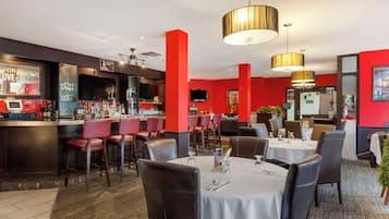 Un restaurante con paredes rojas, una zona de bar y mesas dispuestas para comer.